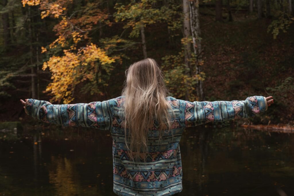 pexels photo 28824976 28824976 Back view of woman embracing nature with open arms in forest during fall.